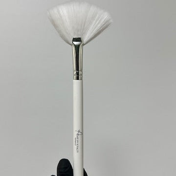 Makeup brush with white bristle head held by a hand wearing a black glove on a gray background